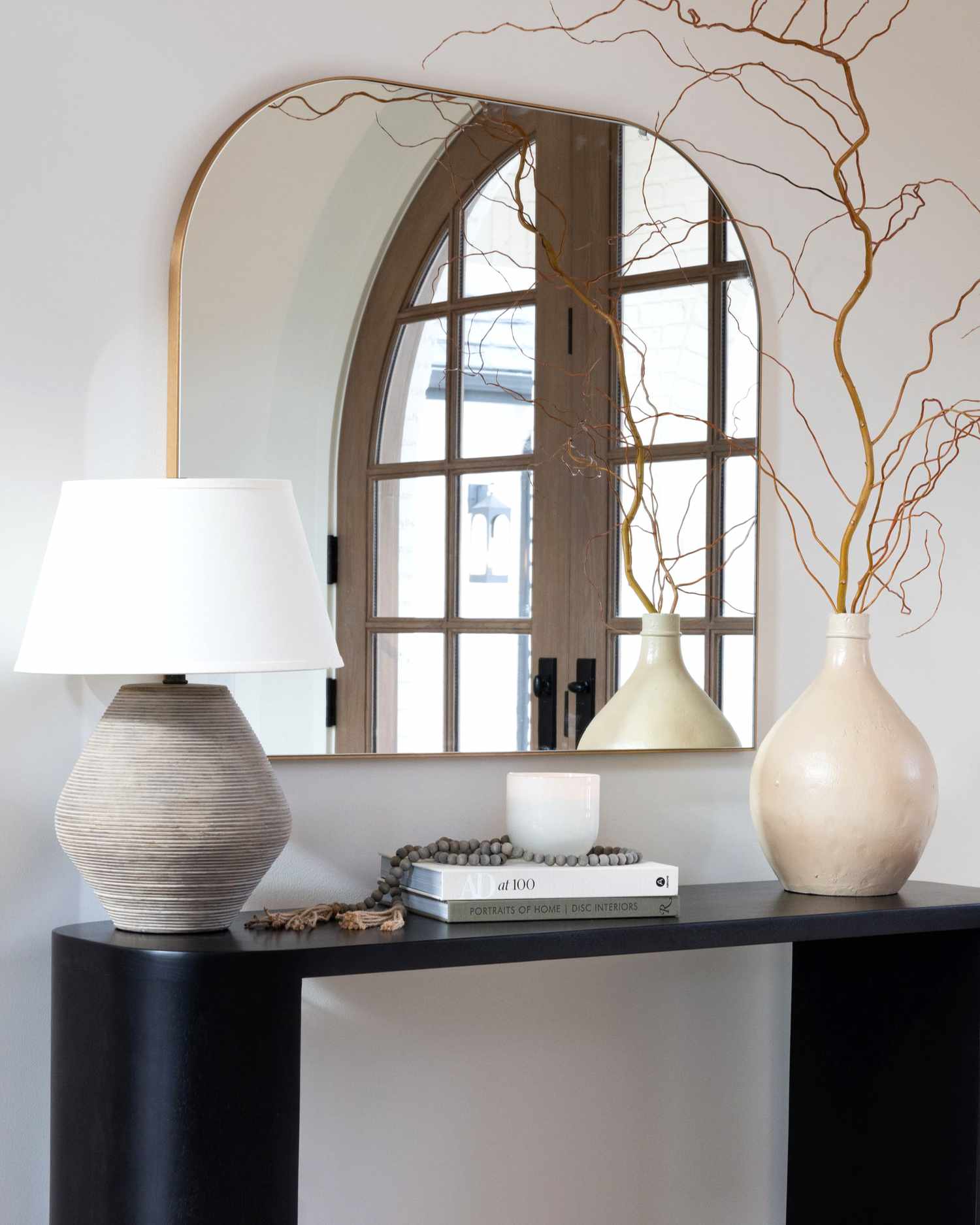 gold mirror above a black console table with lamp and vase