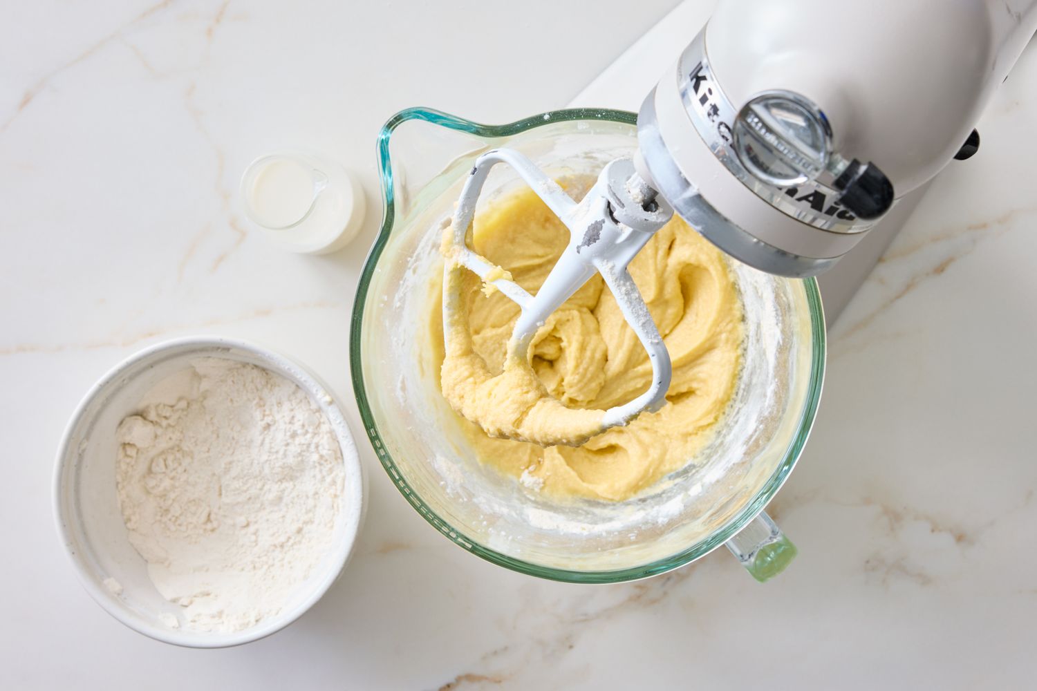 A mixer with batter in a bowl next to a bowl of dry ingredients