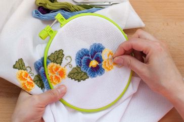 Hands working on embroidery of flowers using a needle and thread