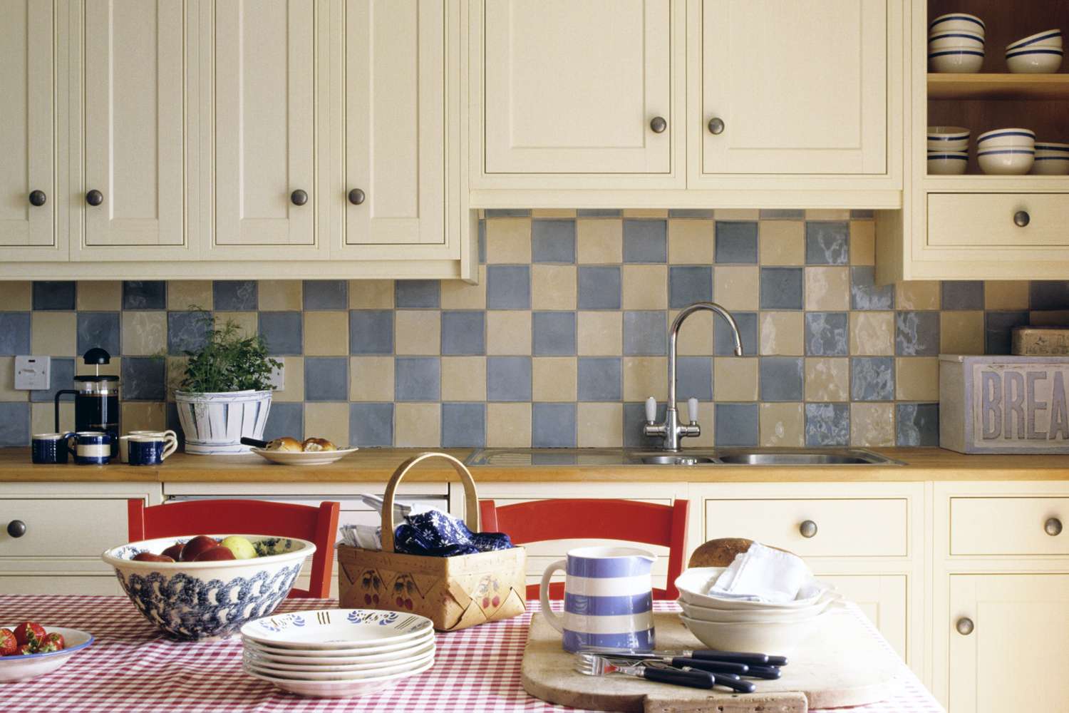 Kitchen with cabinets tiled backsplash and countertop items including dishes on a checkered tablecloth and a basket