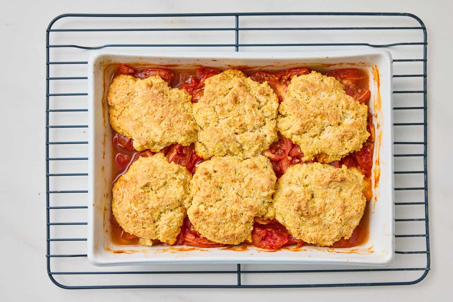 Tomato cobbler with biscuit topping in a baking dish on a cooling rack