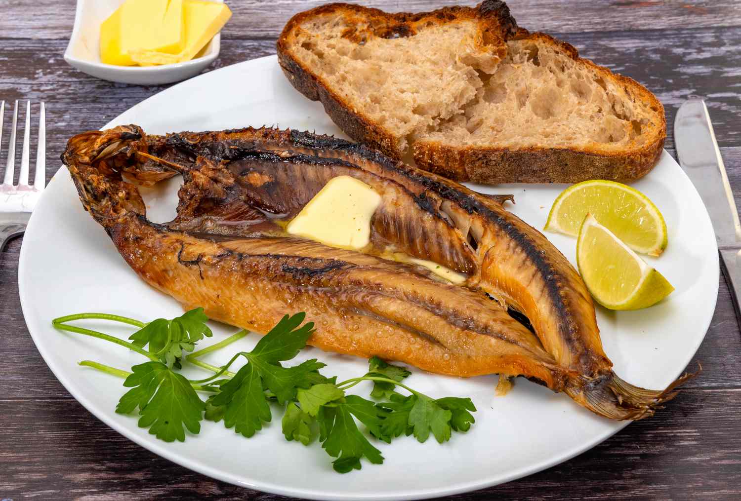 kipper with butter on plate with bread and lemon and parsley
