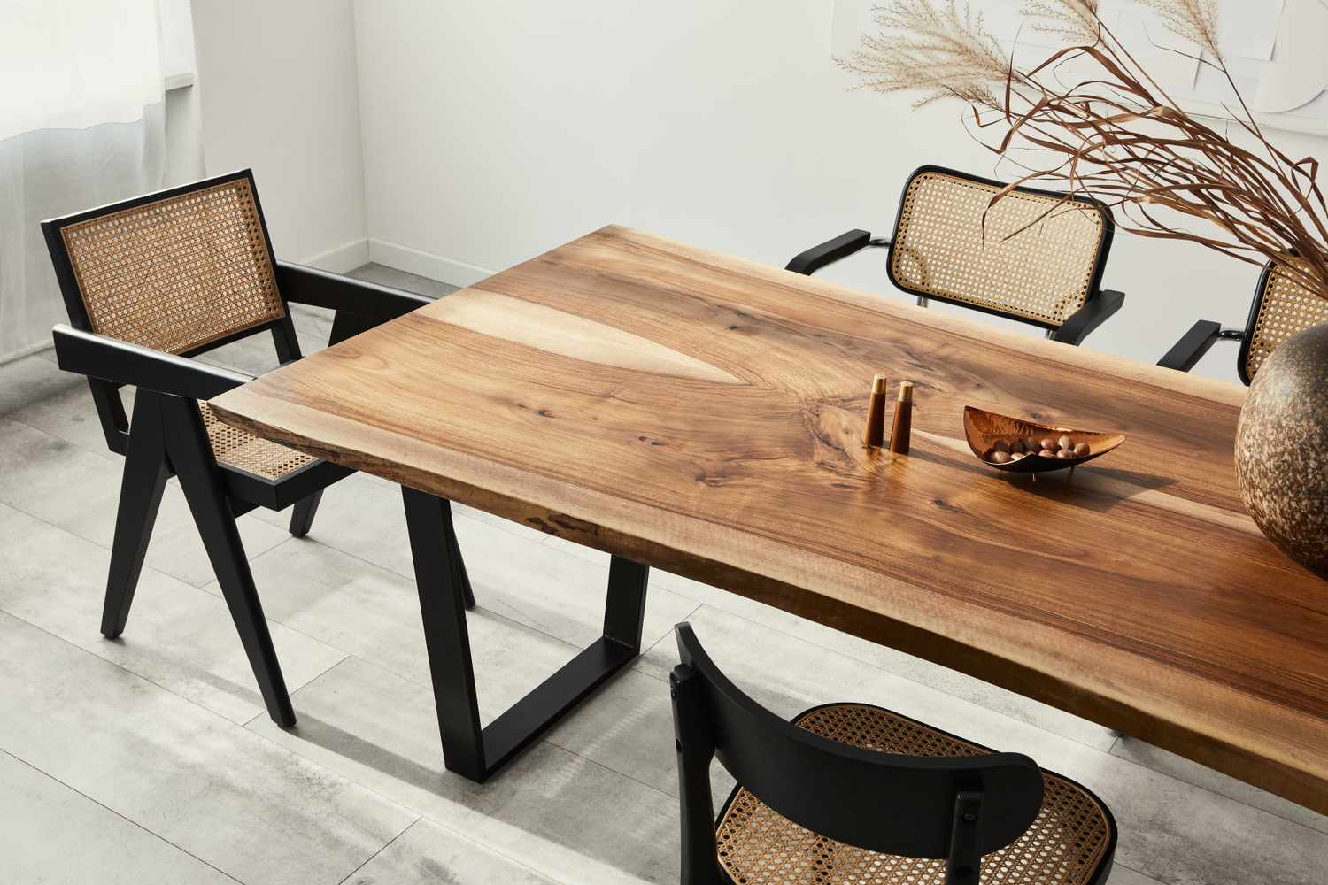 A wooden dining table with modern chairs decorated with copper accents and a vase arrangement