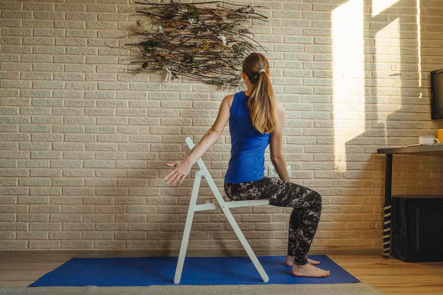 A person performing a seated yoga twist on a chair in a bright room