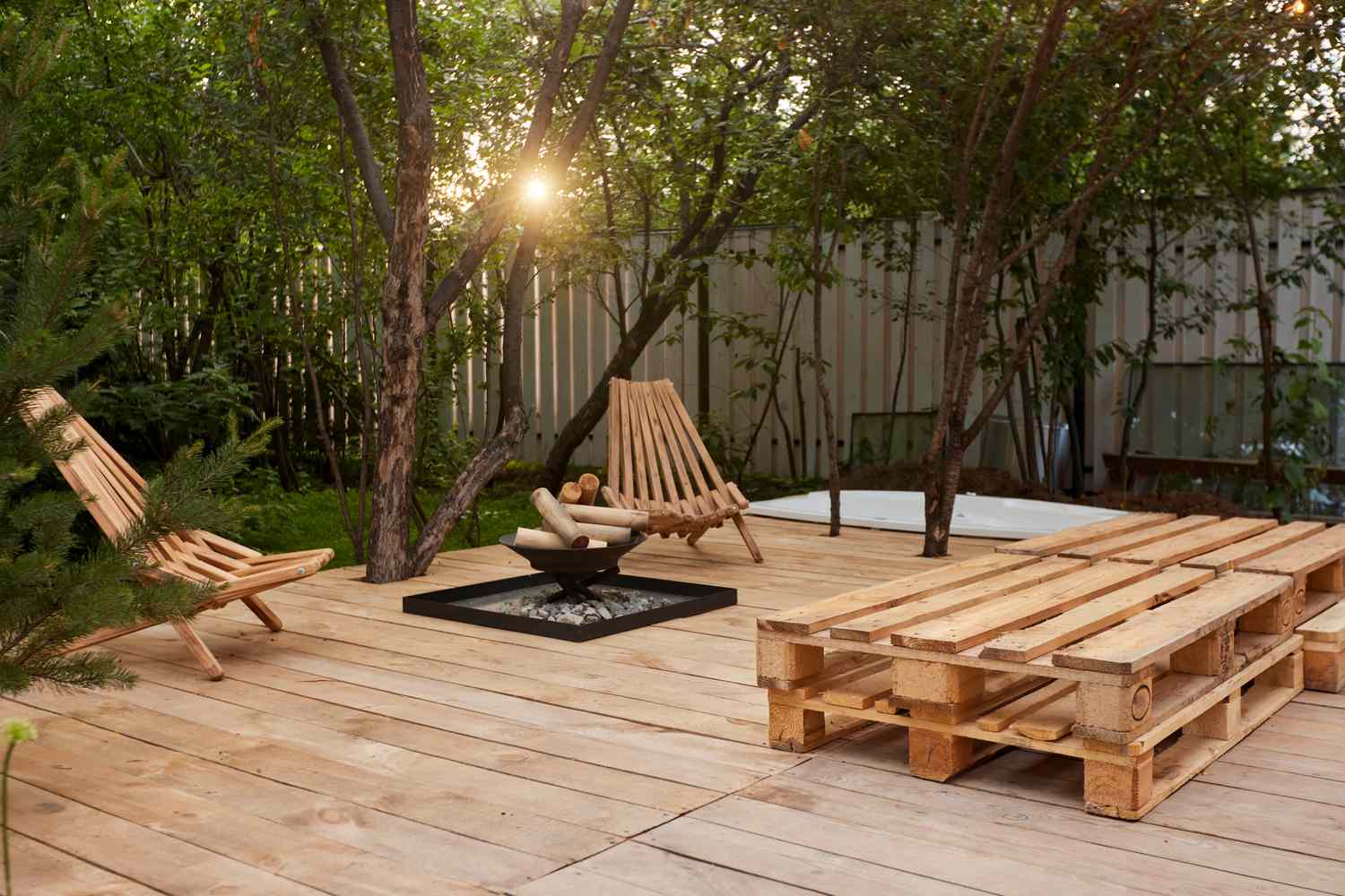 Fire place on a wooden veranda next to chairs and pallets in the garden at sunset. Modern backyard patio with fireplace, back yard design concept