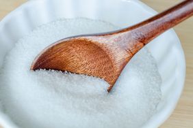 A wooden spoon placed on a bowl of granular white substance likely salt