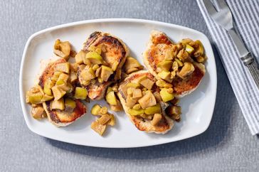 Boneless pork chops topped with apple chutney on a plate accompanied by a striped napkin and utensils nearby