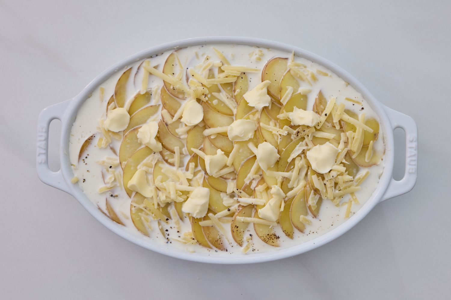 Dish of uncooked scalloped potatoes with cheese and sauce in a white baking dish