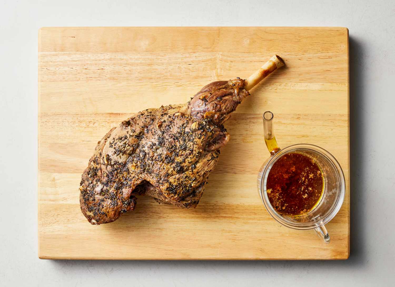 cooked leg of lamb on cutting board with vessel of meat juices