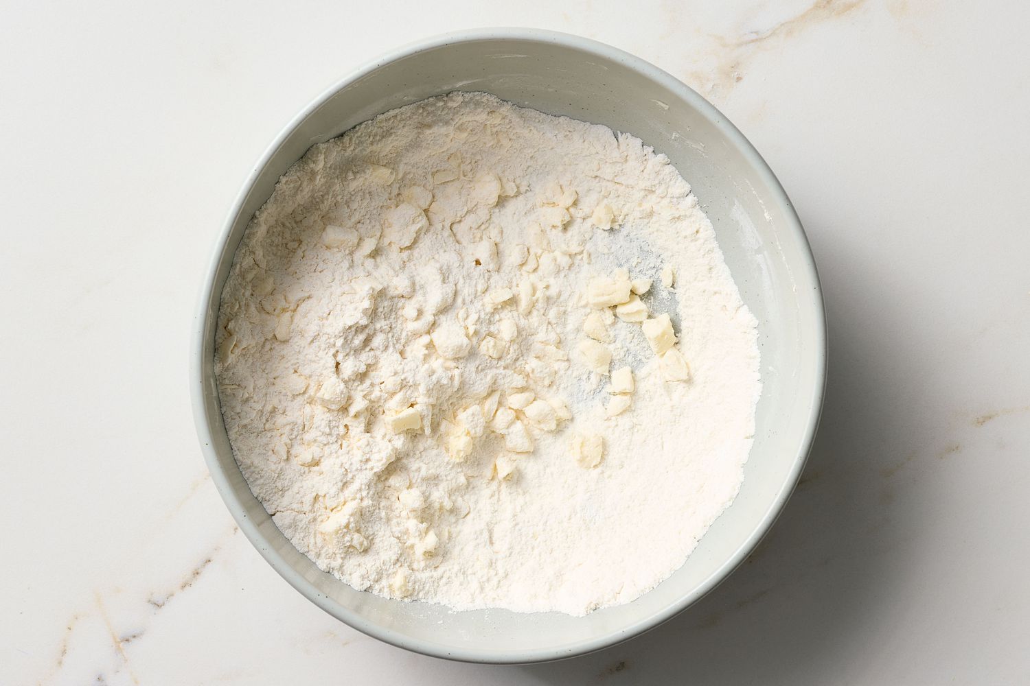 A bowl containing a dry mixture with small butter pieces, ingredients for a dessert preparation