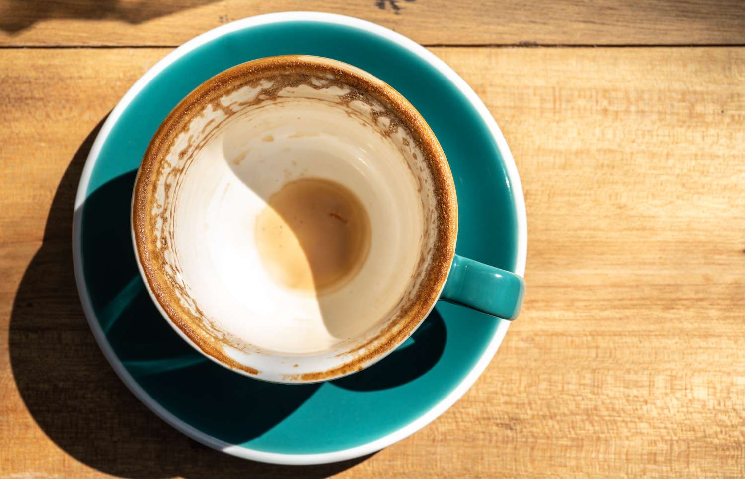 An empty coffee cup with residue sits on a saucer on a wooden table