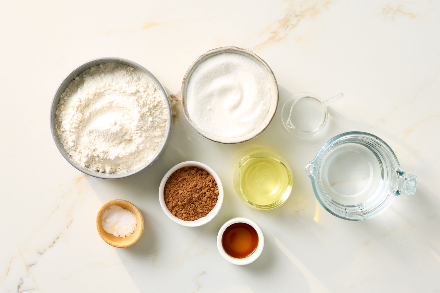 Ingredients for a chocolate cake including flour sugar cocoa powder oil vanilla salt and water arranged on a surface