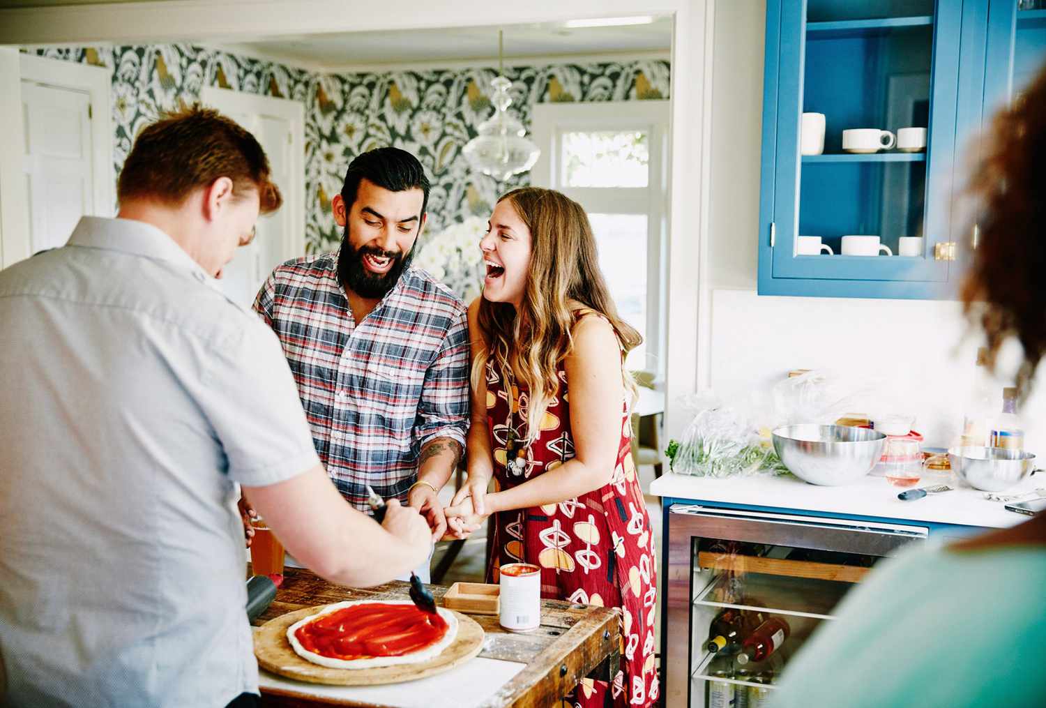Laughing couple preparing pizza together with friends in kitchen