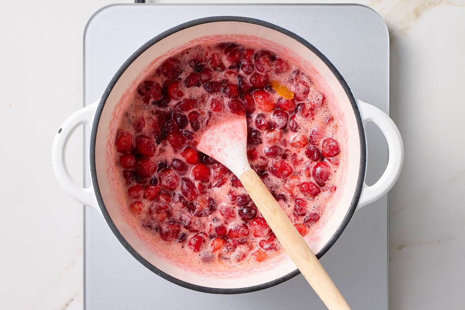 Cranberry sauce being cooked in a pot on a stove with a spoon