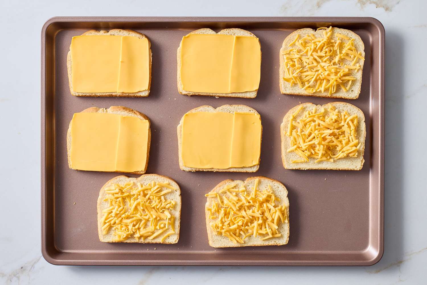 Slices of bread topped with sliced cheese and shredded cheese placed on a baking tray preparation for making grilled cheese sandwiches
