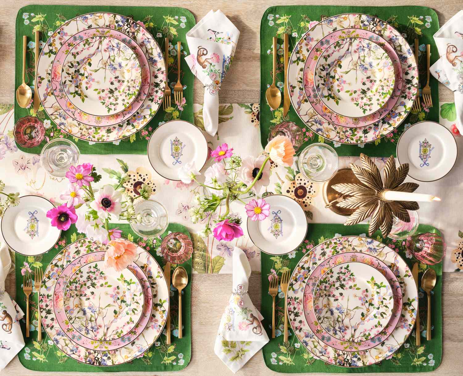 A floral-themed table setting for four with decorated plates, gold utensils, and a centerpiece of flowers