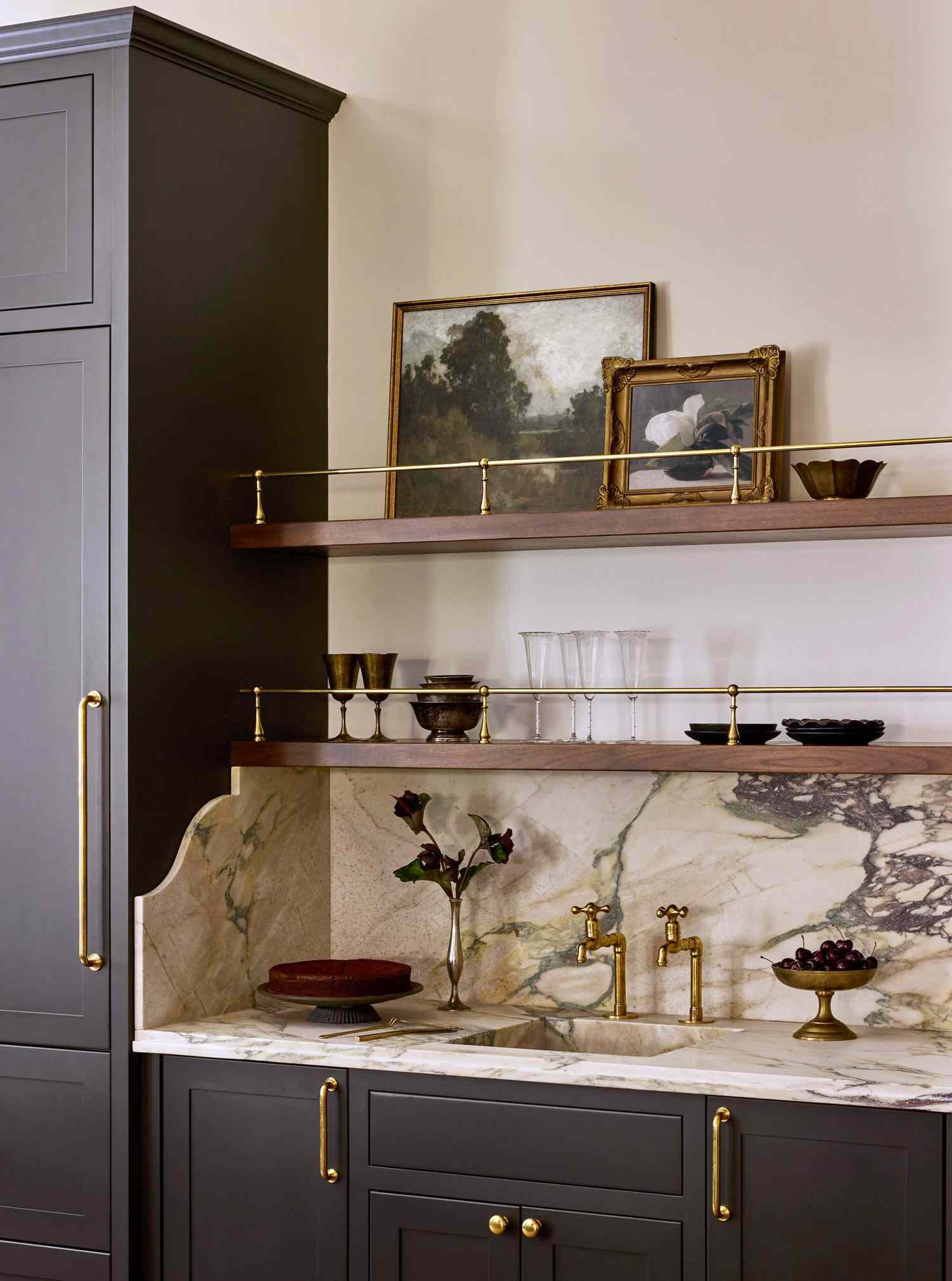 Kitchen cabinet with a marble countertop, shelving with decorative items and framed pictures, golden hardware details