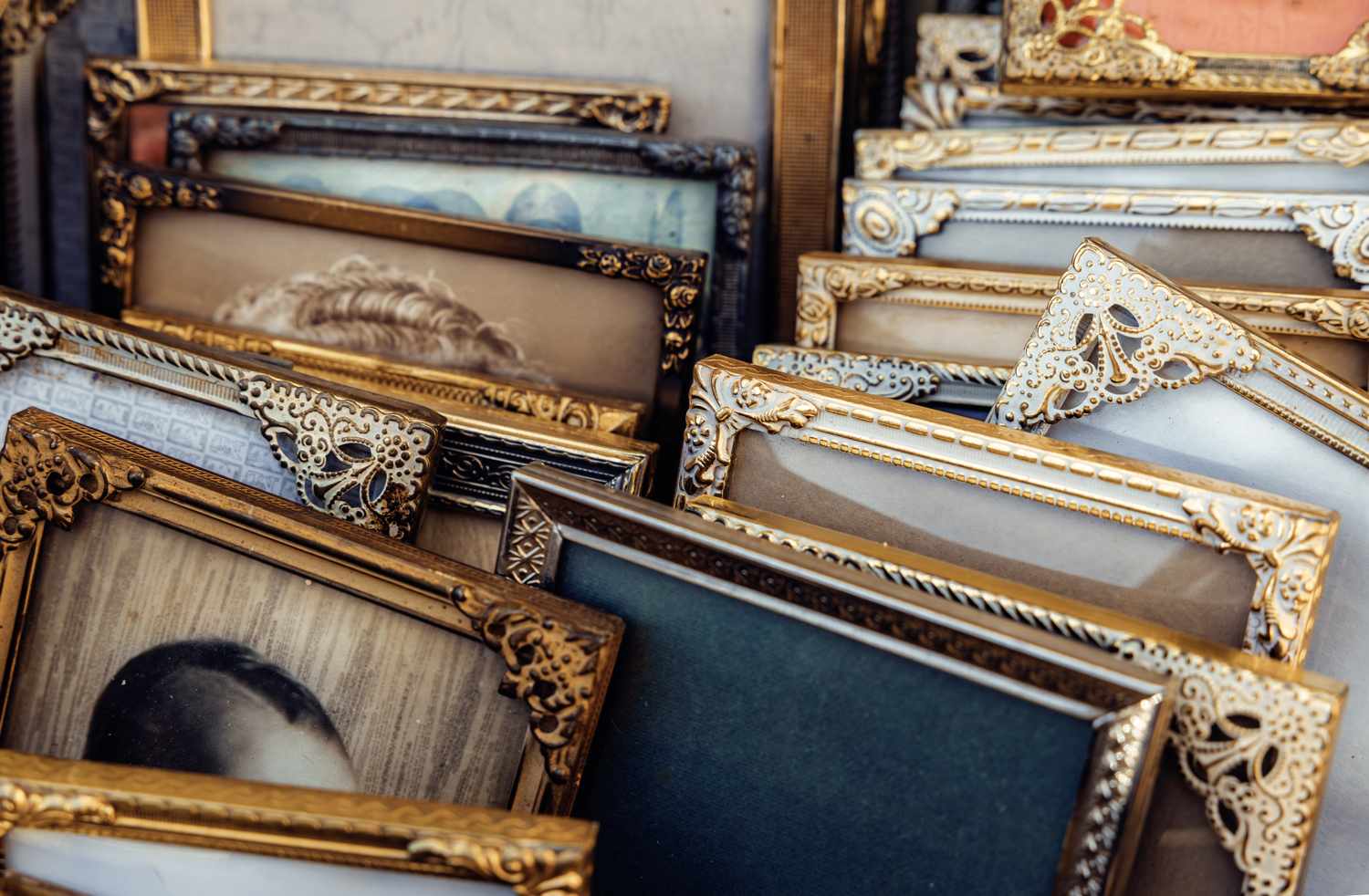 Vintage gilded picture frames with ornate carved details and faded portraits displayed at an outdoor flea market stall, evoking nostalgia, heritage, and timeless elegance