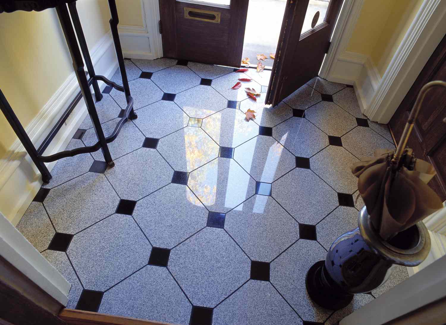 Tiled floor near an open front door with sunlight reflecting on the tiles and a few leaves scattered inside