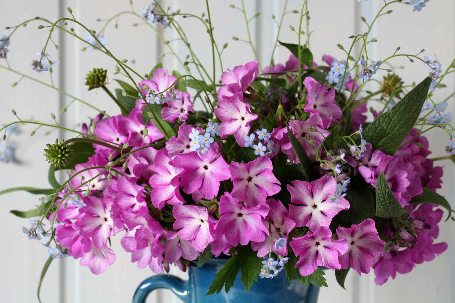 A bouquet of flowers arranged in a blue vase featuring a mix of pink and white blossoms with green foliage