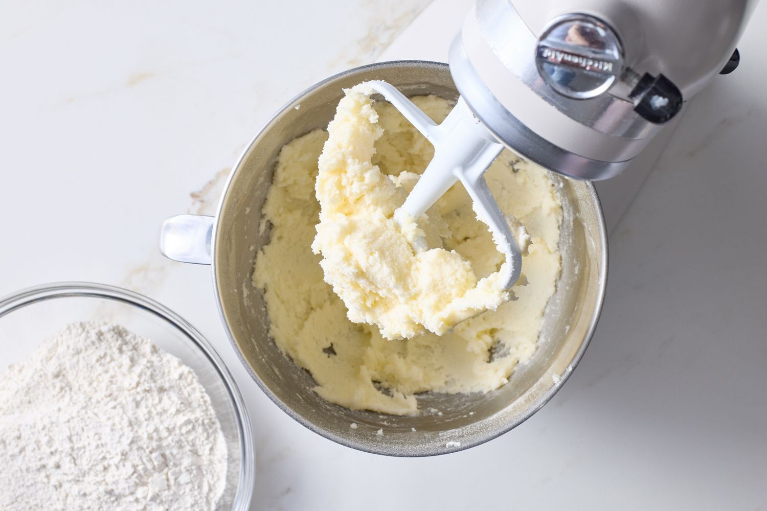 Butter and sugar being creamed in a stand mixer bowl with a bowl of flour next to it preparing cupcake batter