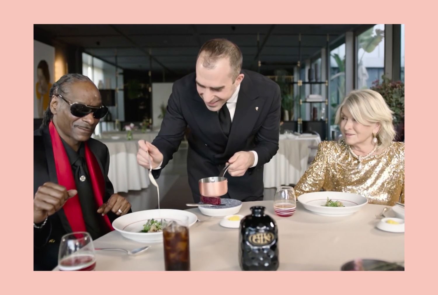 Snoop Dogg and decorvow at a dinner table with a waiter serving food