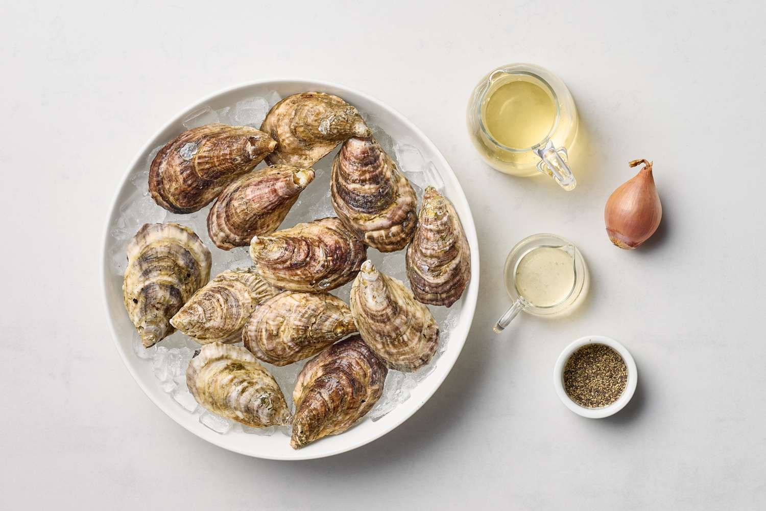 A plate of oysters on ice surrounded by mignonette ingredients including shallots vinegar and pepper