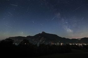 Night sky with a meteor shower silhouetted mountains with distant lights below