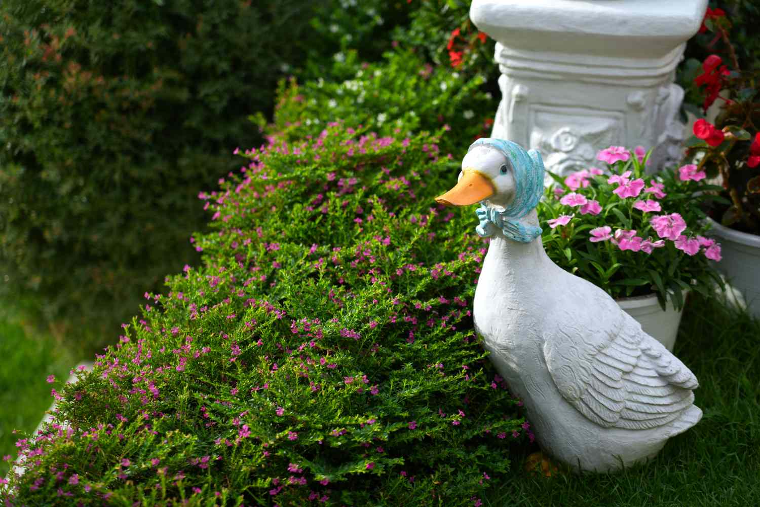 Decorative statue of a duck wearing a bonnet placed among flowers and greenery in a garden setting