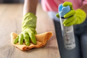 A person wearing gloves cleaning a wooden surface with a spray and cloth