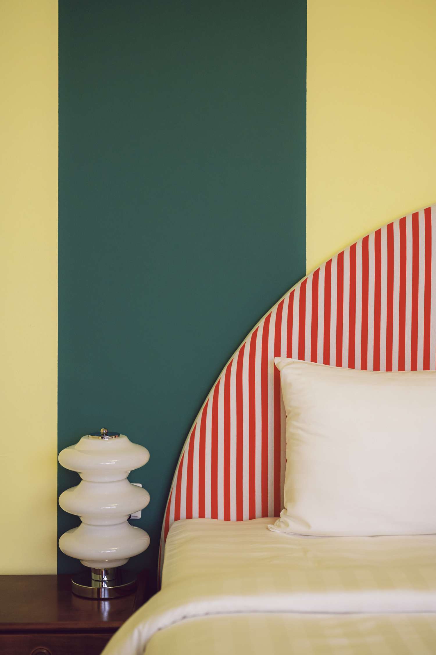 A modern bedroom interior with a striped headboard and decorative table lamp