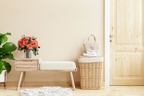 A stylish room with a bench a wicker basket and a vase of flowers near a wooden door