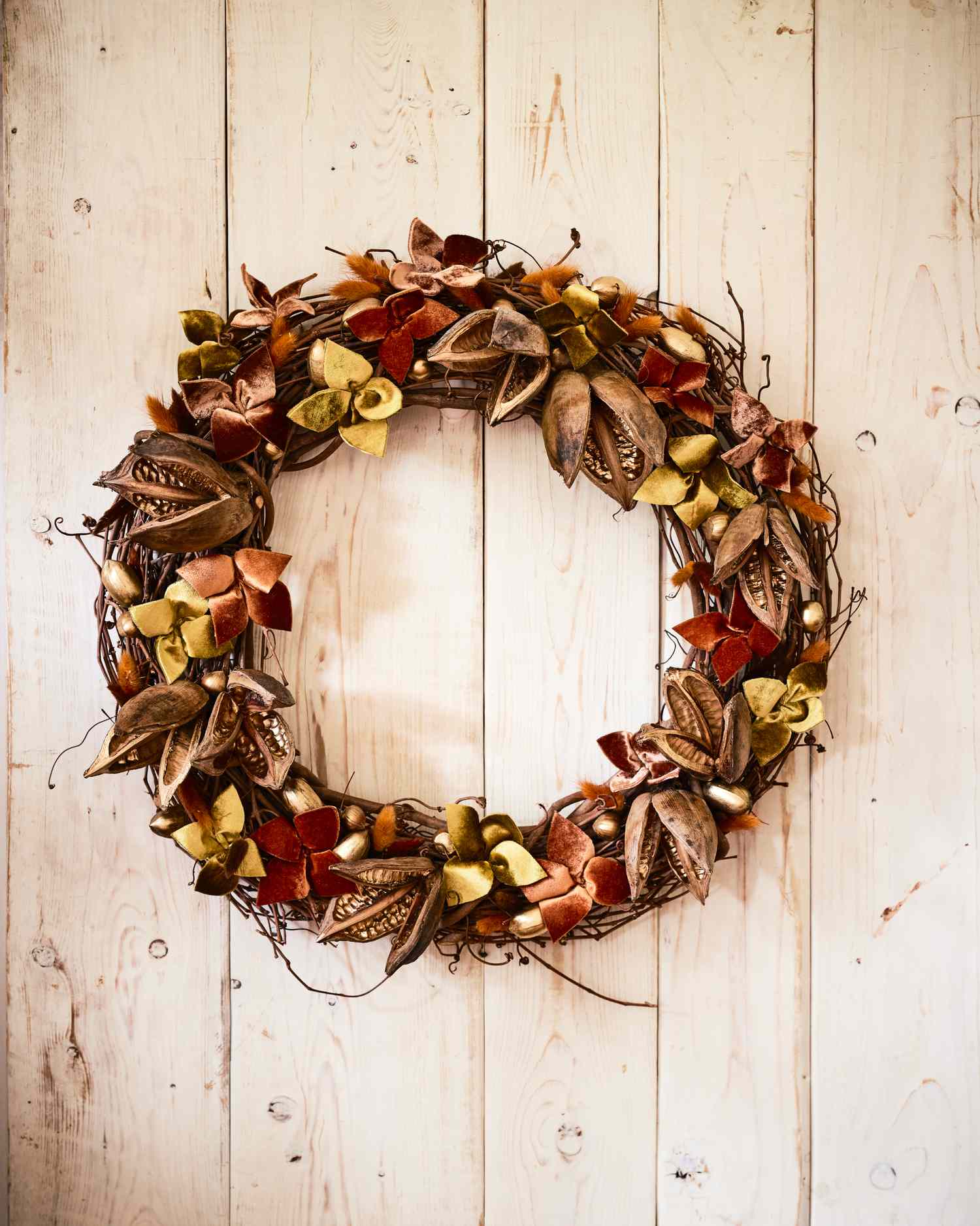 A wreath made of autumn leaves and accents displayed on a wooden wall