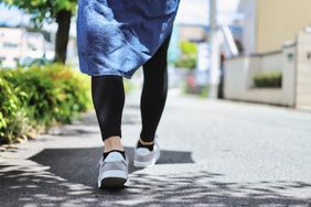 A person walking outdoors on a sidewalk lower legs and feet visible in casual attire