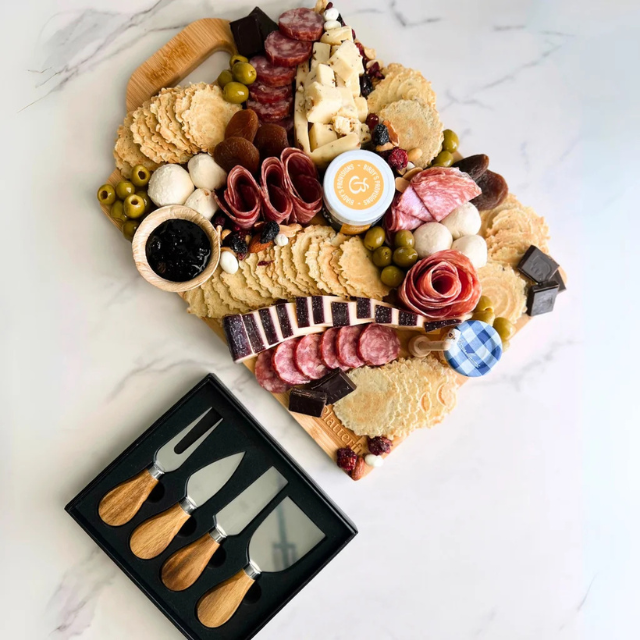Charcuterie board with meats cheeses fruits crackers and a cheese knife set displayed beside it