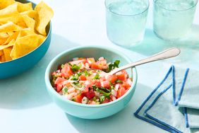 Bowl of salsa fresca with a spoon, tortilla chips in a separate bowl, and glasses of water nearby