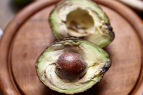 Two avocado halves on a wooden surface one displaying the seed in the center and the other without