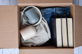 An open cardboard box containing items like mugs, folded clothes, and books for donation