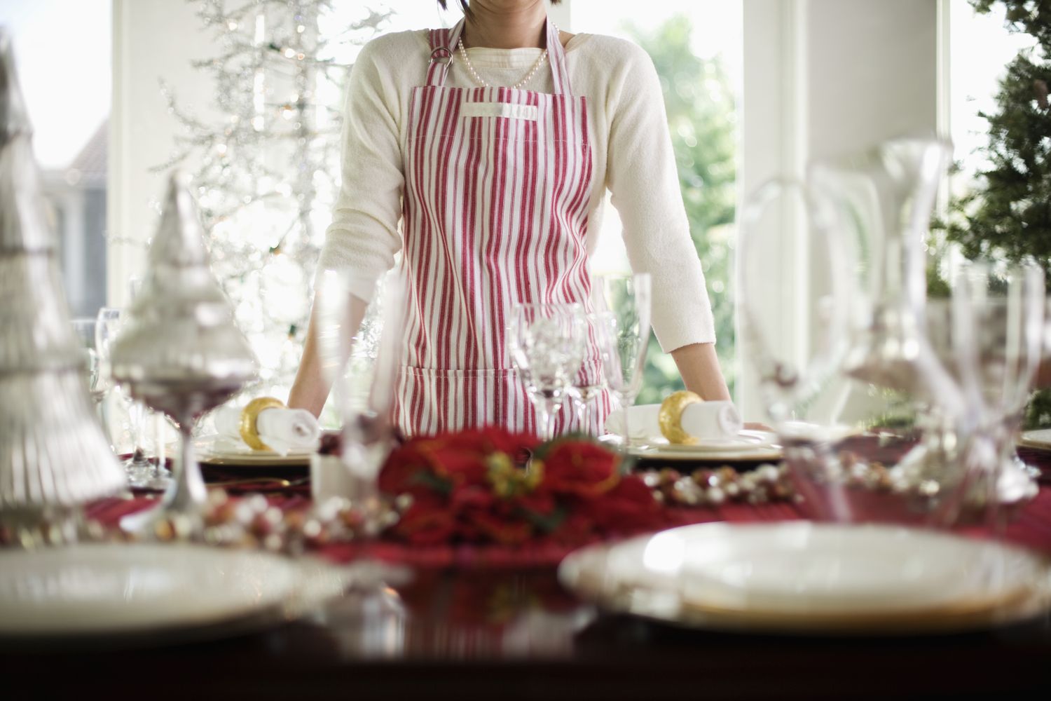 Person wearing a striped apron standing behind a decorated dining table with holidaythemed centerpiece and tableware