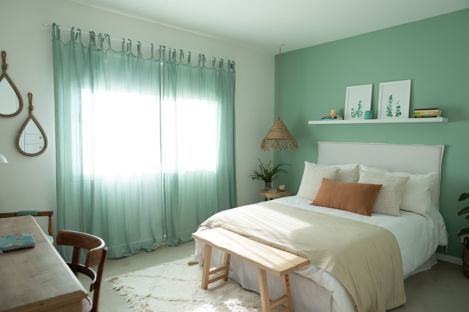A neatly arranged bedroom with a bed green curtains and minimalist decor