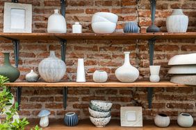 Shelves displaying various ceramic vases and bowls placed against a brick wall