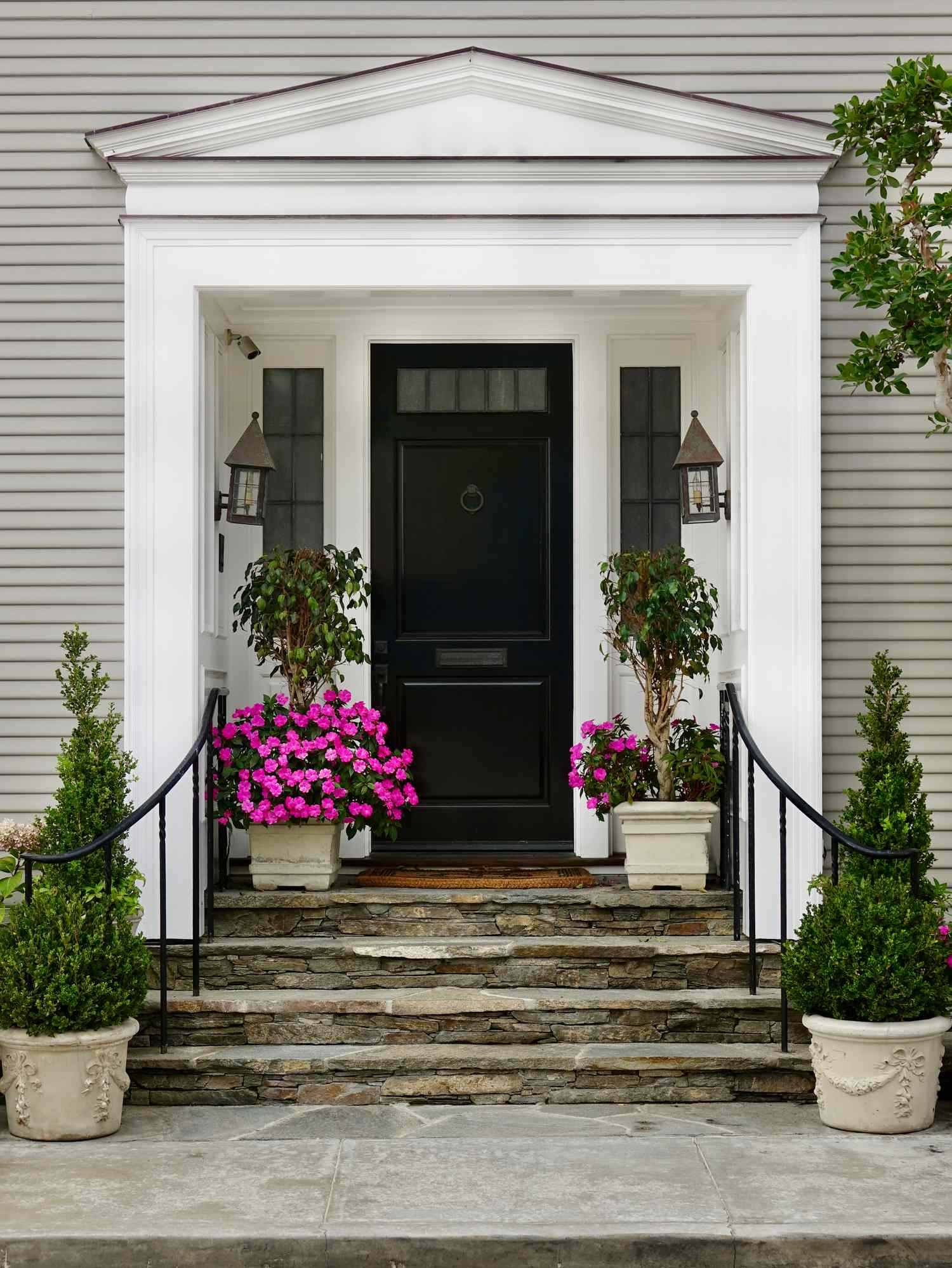 A house front door with a small porch potted plants and two lanternstyle light fixtures