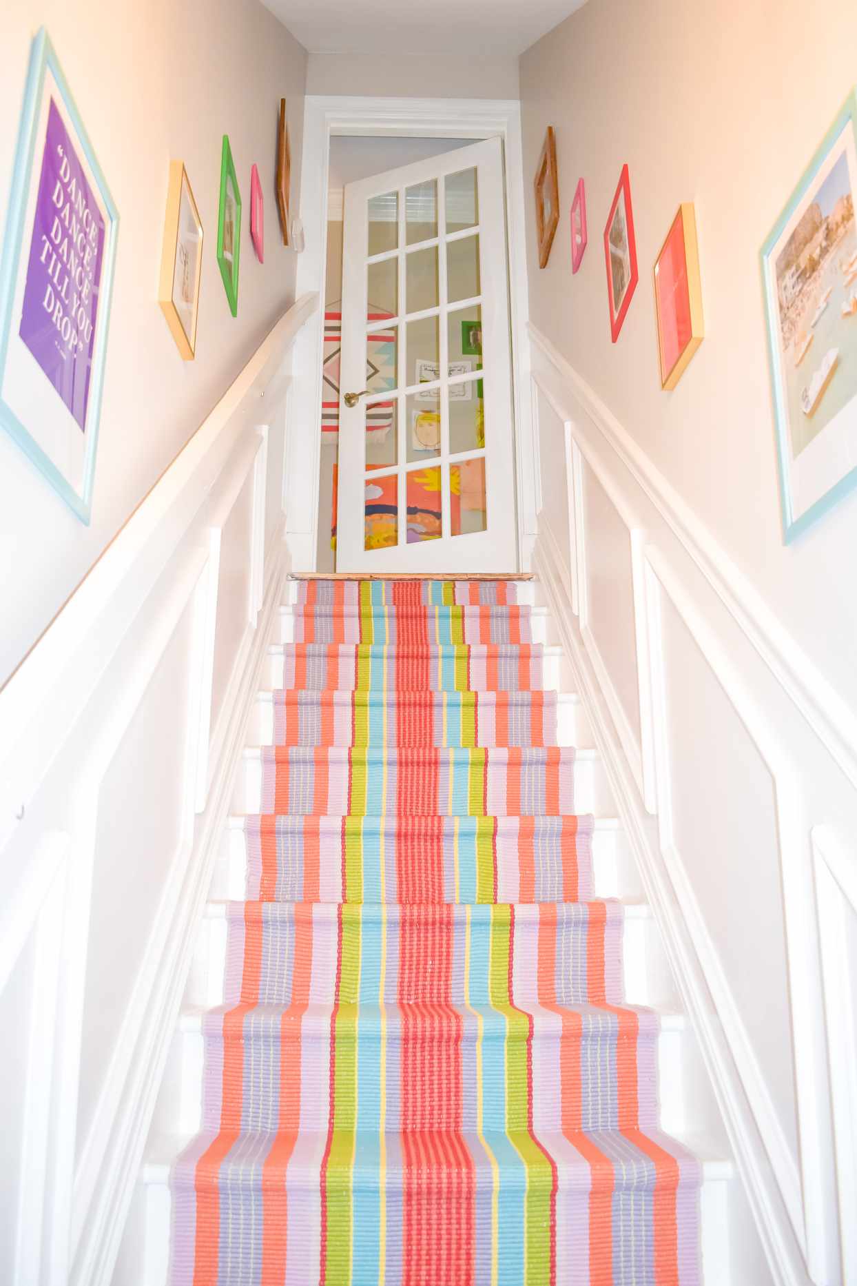 basement stairs with art lining walls and a colorful carpet runner