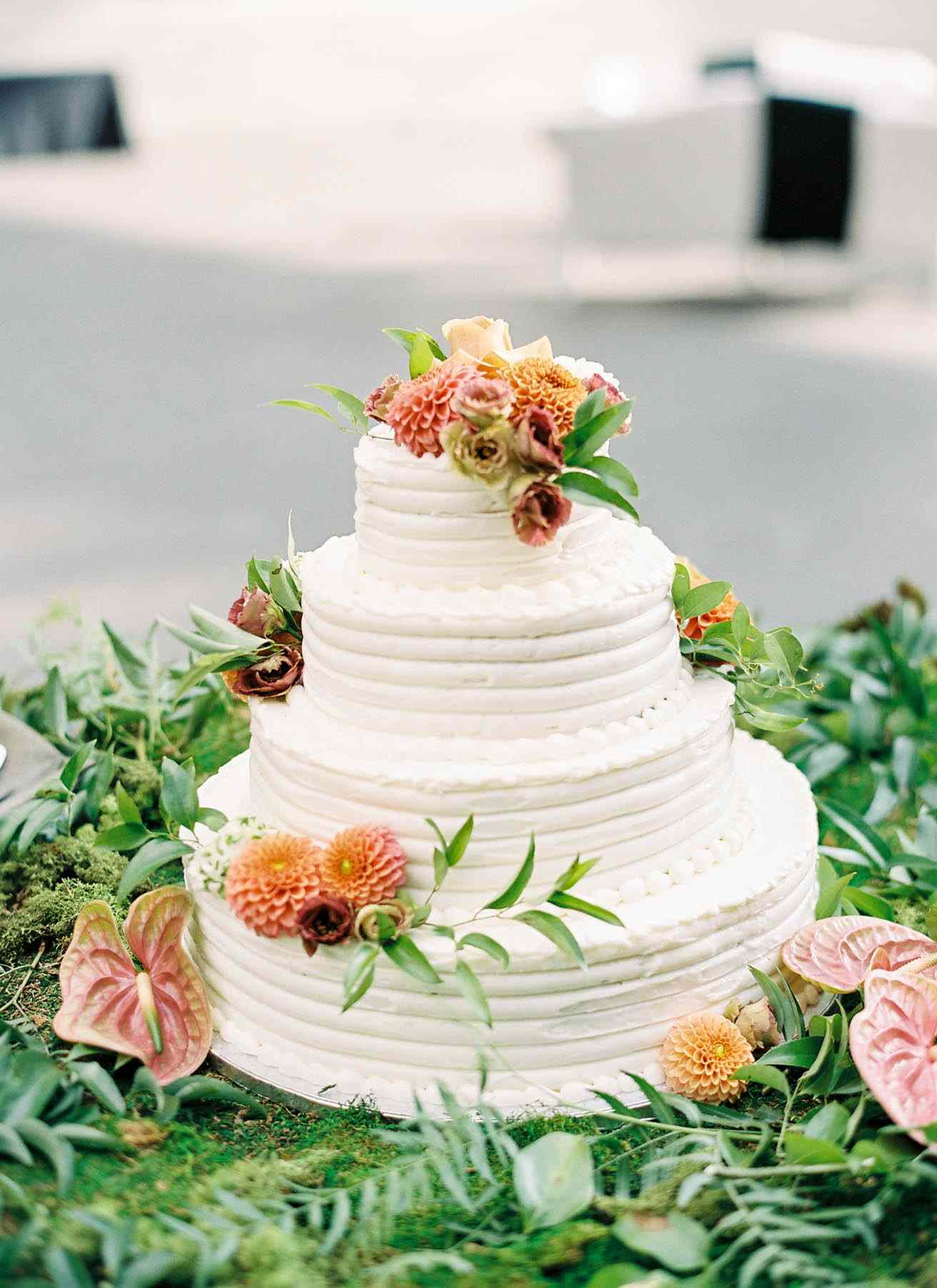 wedding cake topped with florals and surrounded by greenery