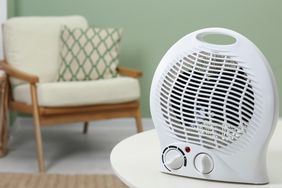 A portable space heater on a table with a chair and cushion in the background
