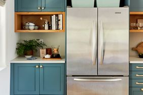 A stainless steel refrigerator in a modern kitchen with teal cabinets