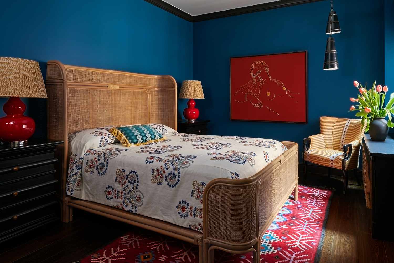 a blue bedroom with cane winged bed frame and a red printed rug 