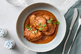 A bowl of chicken mole garnished with herbs set on a table with a knife fork and napkin