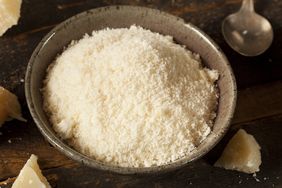 Bowl of grated cheese on a wooden surface with a spoon nearby