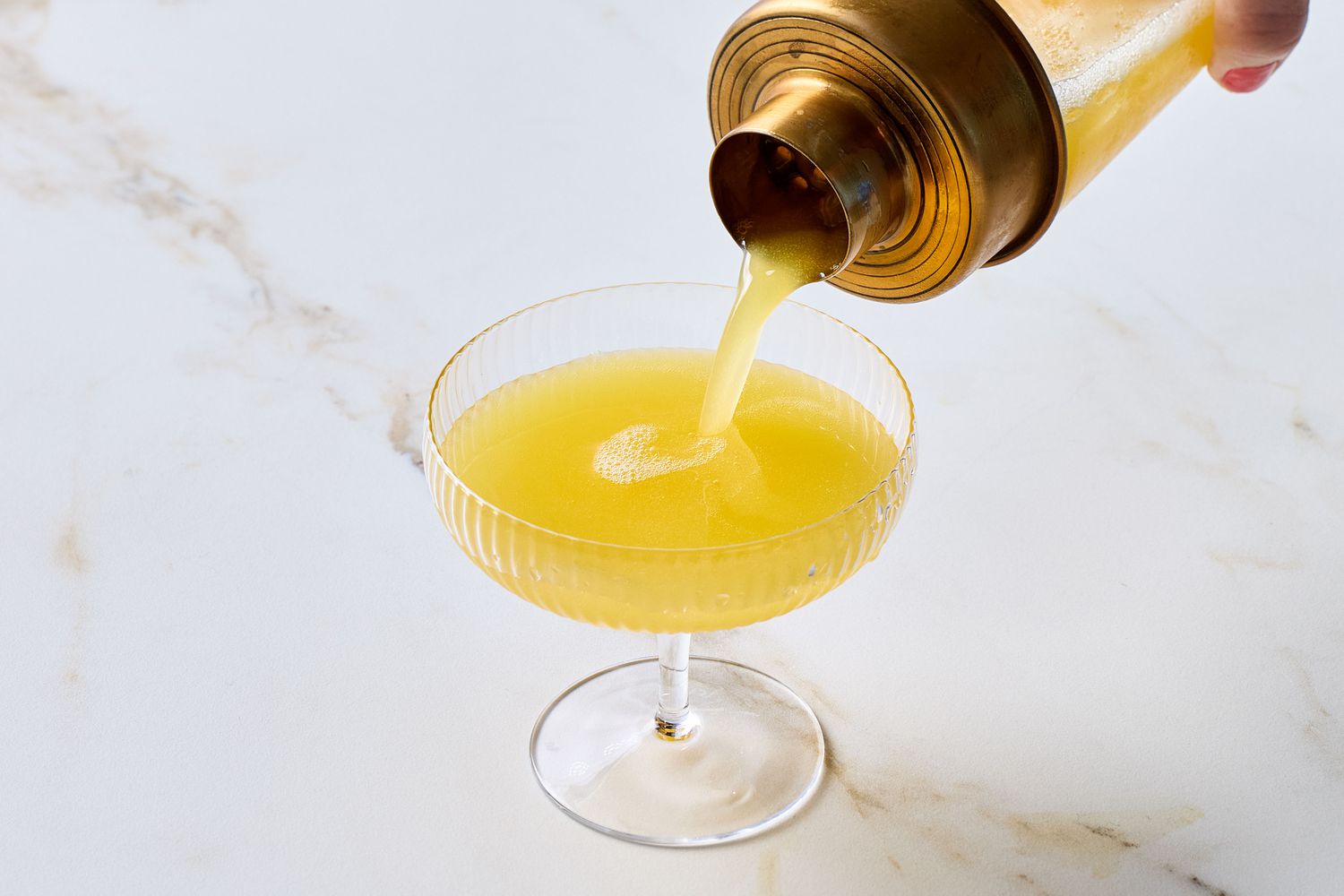 Cocktail being poured into a stemmed glass from a gold shaker